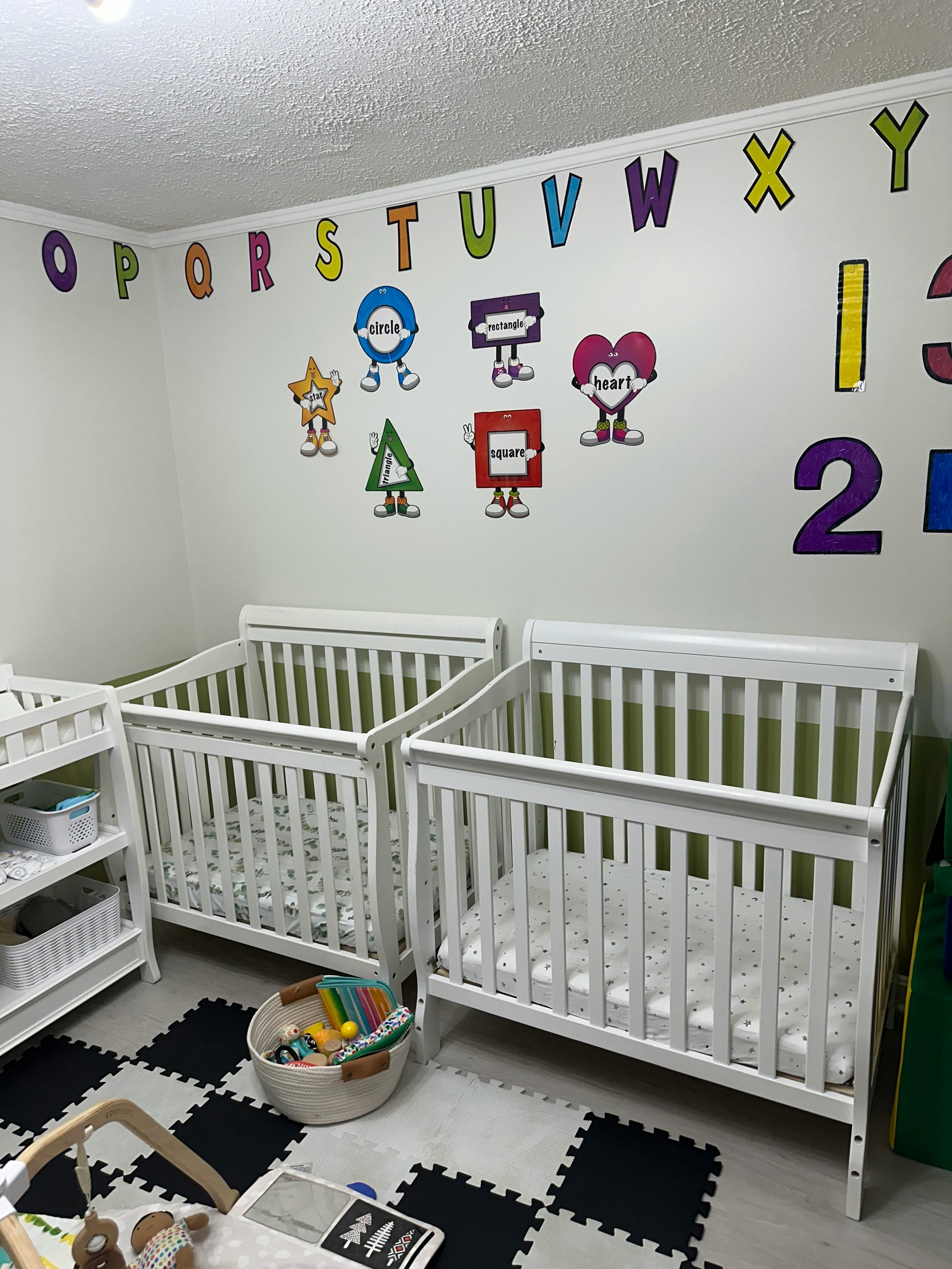 Two white cribs with colorful alphabet and shape decals on the wall