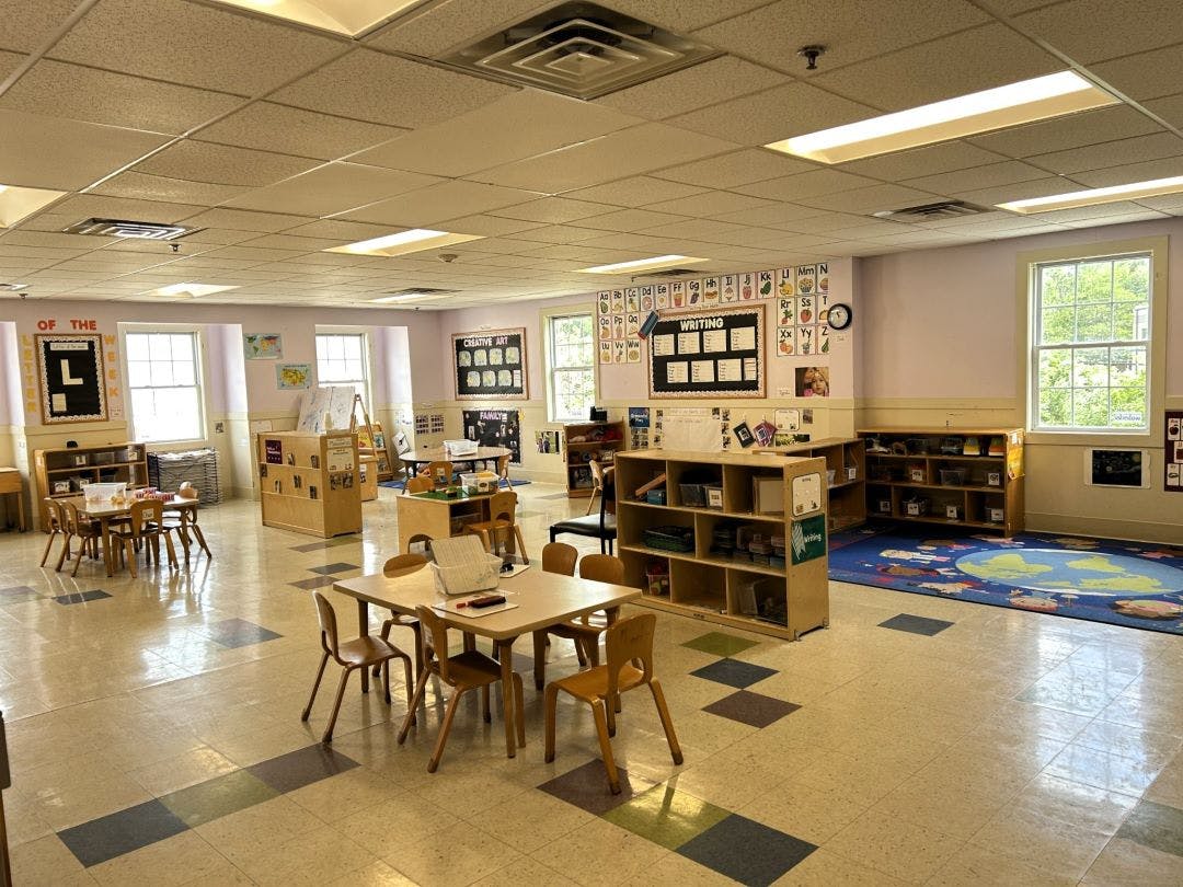 Empty classroom with small tables and chairs, shelves, and educational posters
