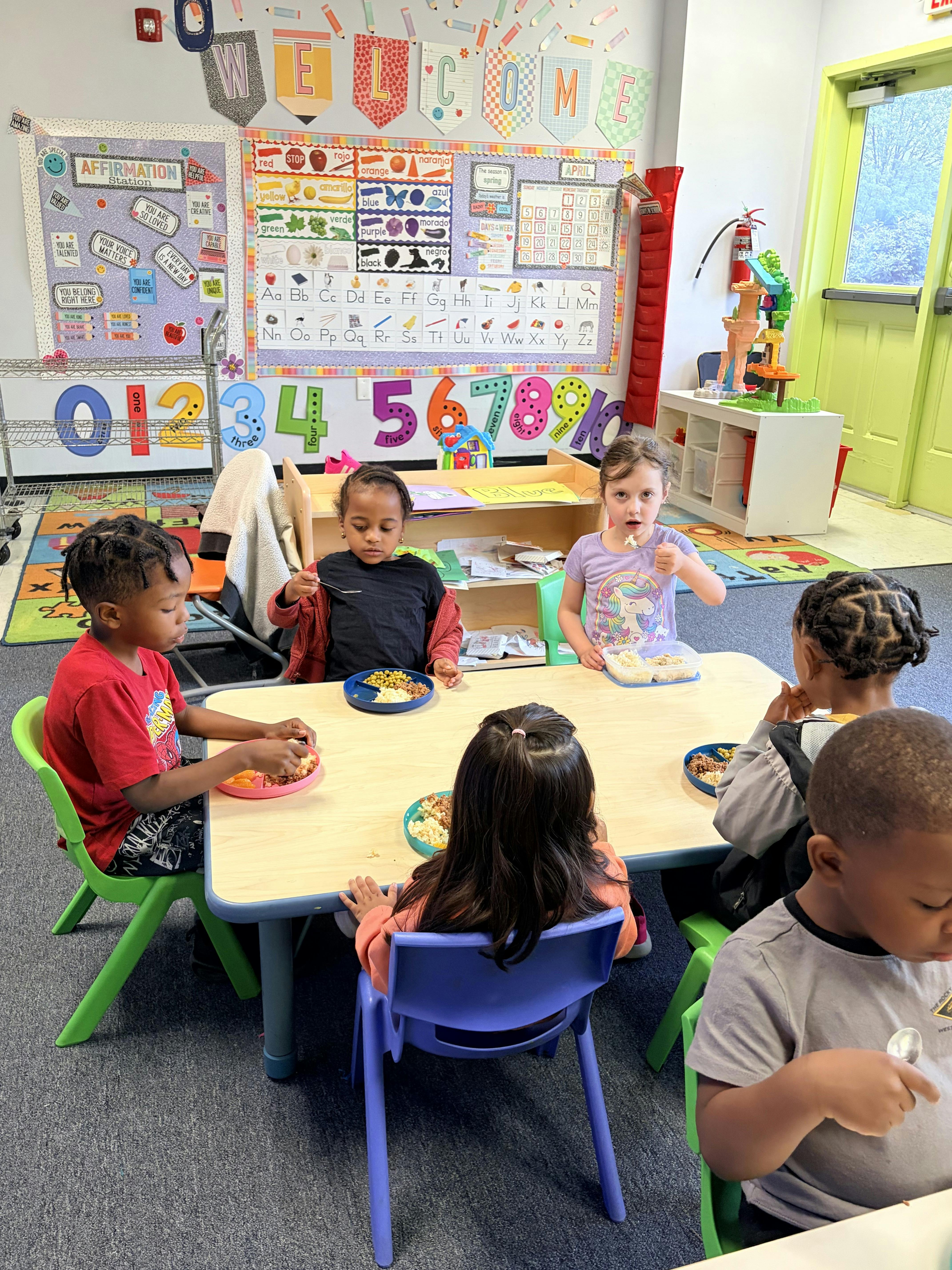 Five children eating at a small table in a classroom