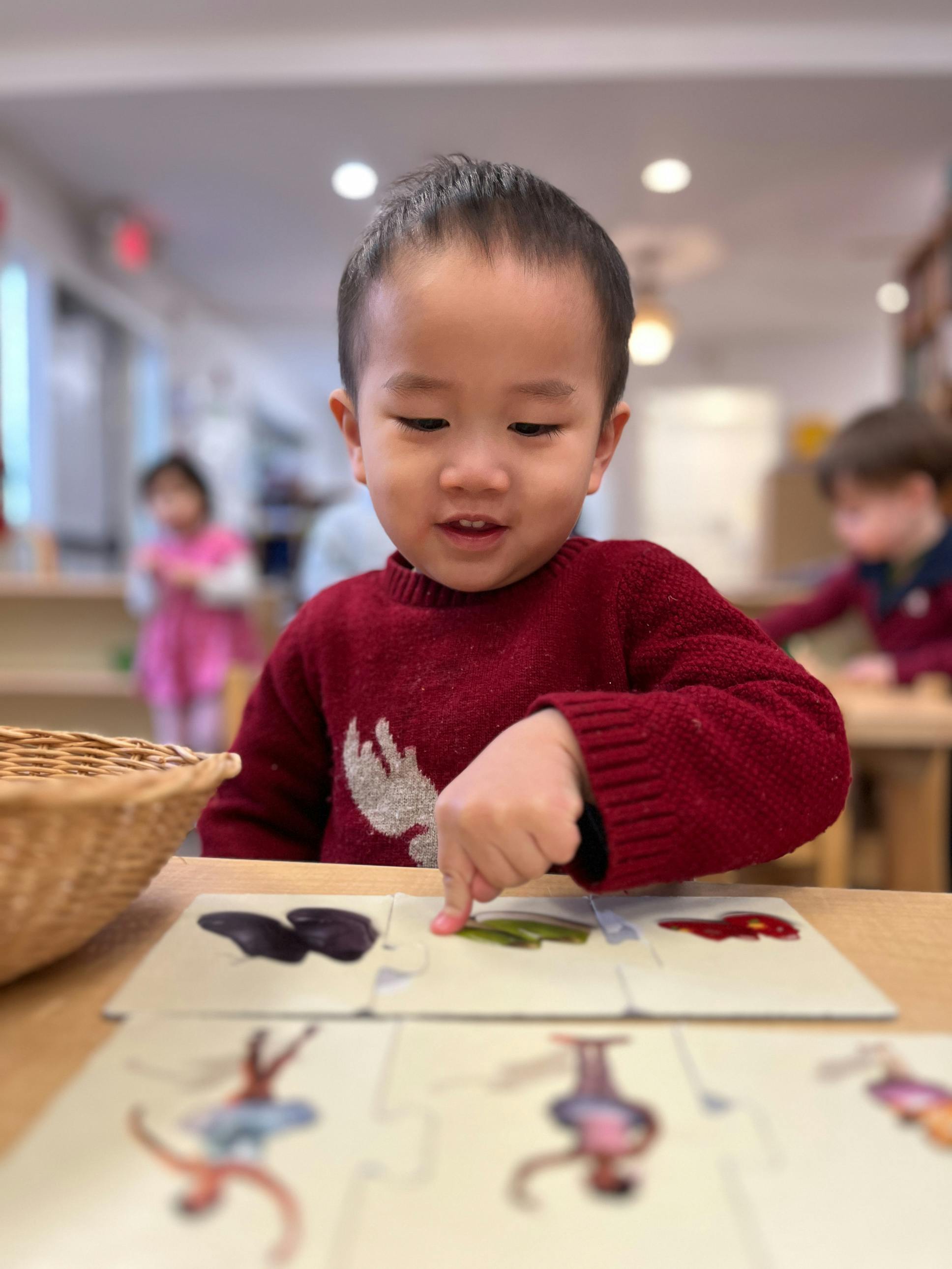 Child in a red sweater pointing at a puzzle piece on a table