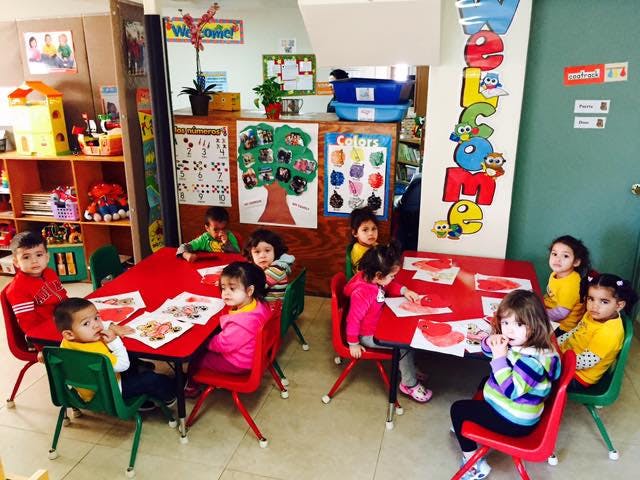 Children sitting at red tables in a classroom