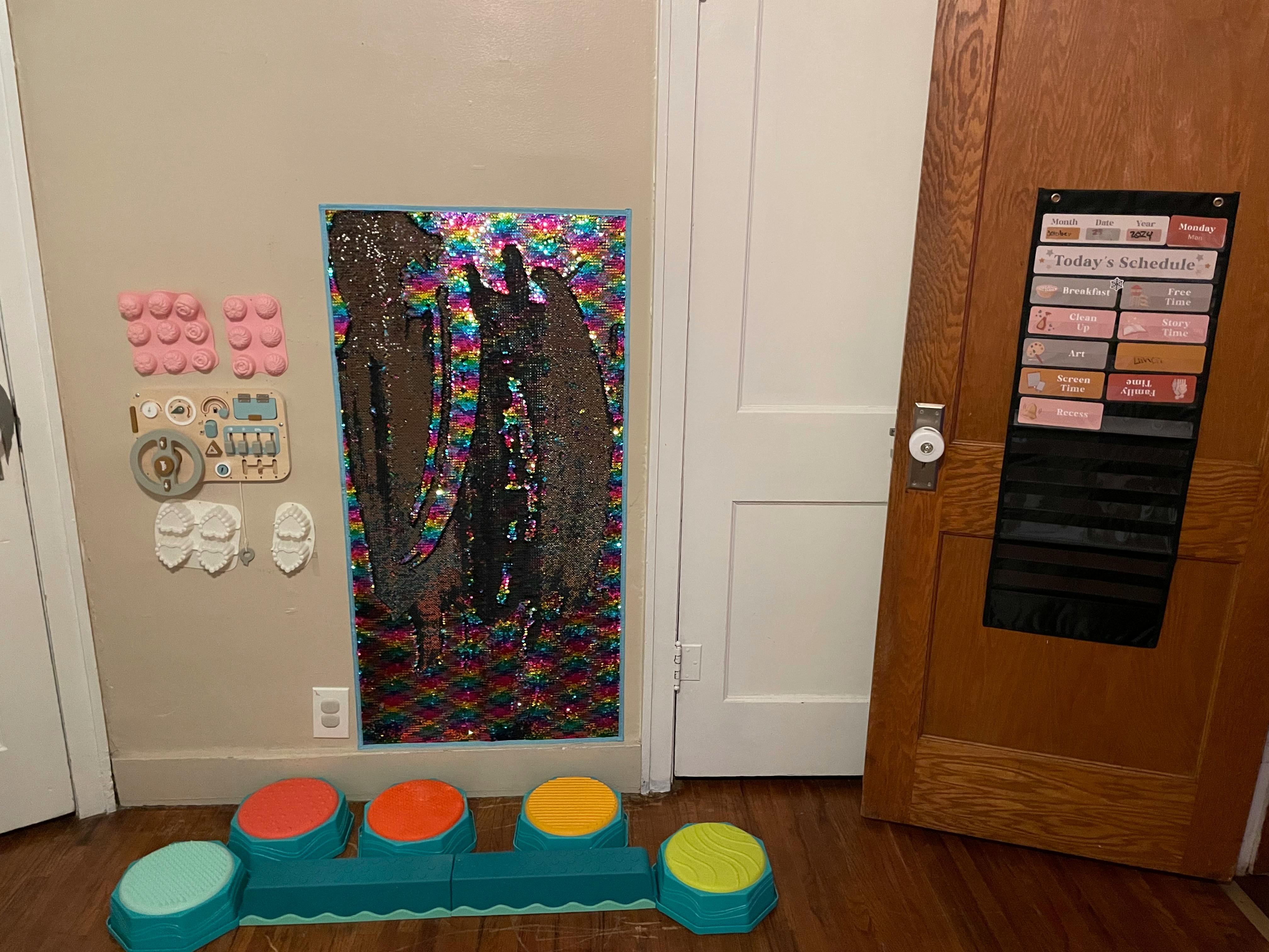 Wall with colorful art, pink shapes, and a wooden door with a hanging organizer