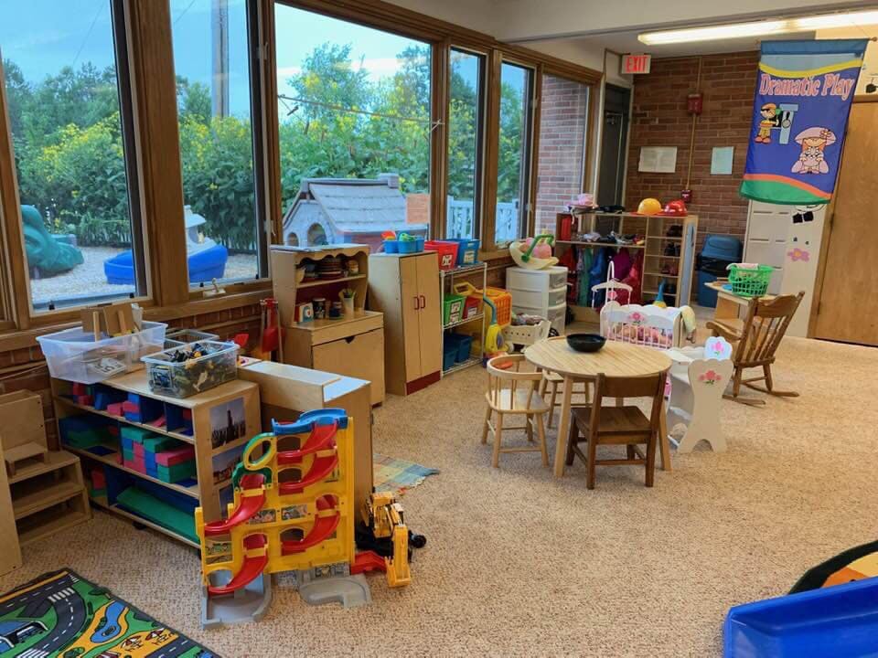 Playroom with tables, chairs, and toys, large windows overlooking an outdoor play area