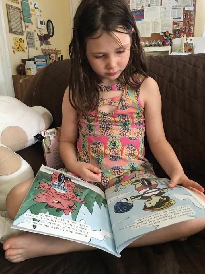Child sitting on a couch reading an open book