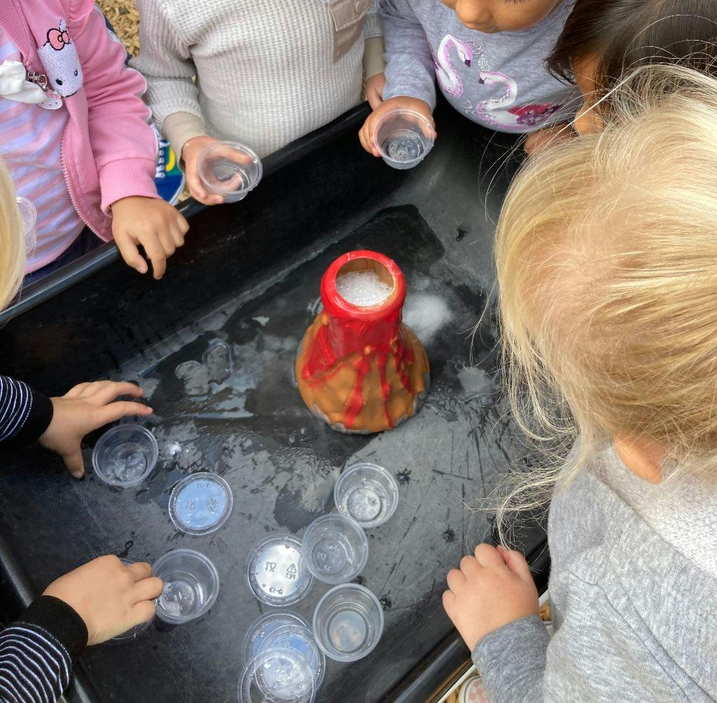 Children gathered around a science experiment with a volcano model