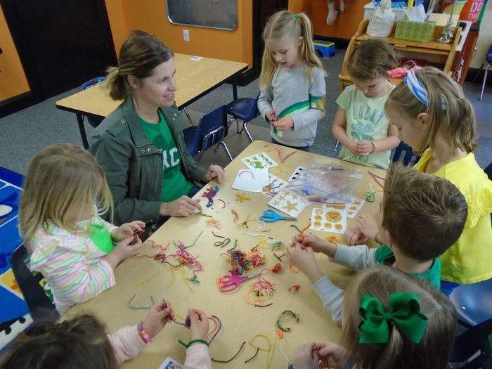 Adult and children making crafts at a table in a classroom