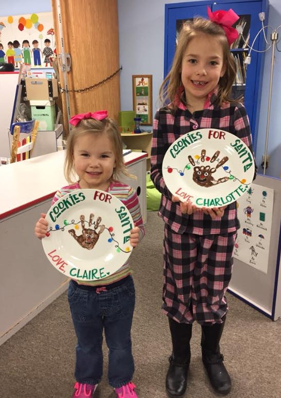 Two children holding plates with handprint reindeer and "Cookies for Santa" text