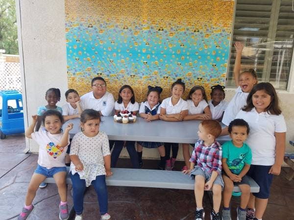 Group of children and adults posing around a table with cupcakes