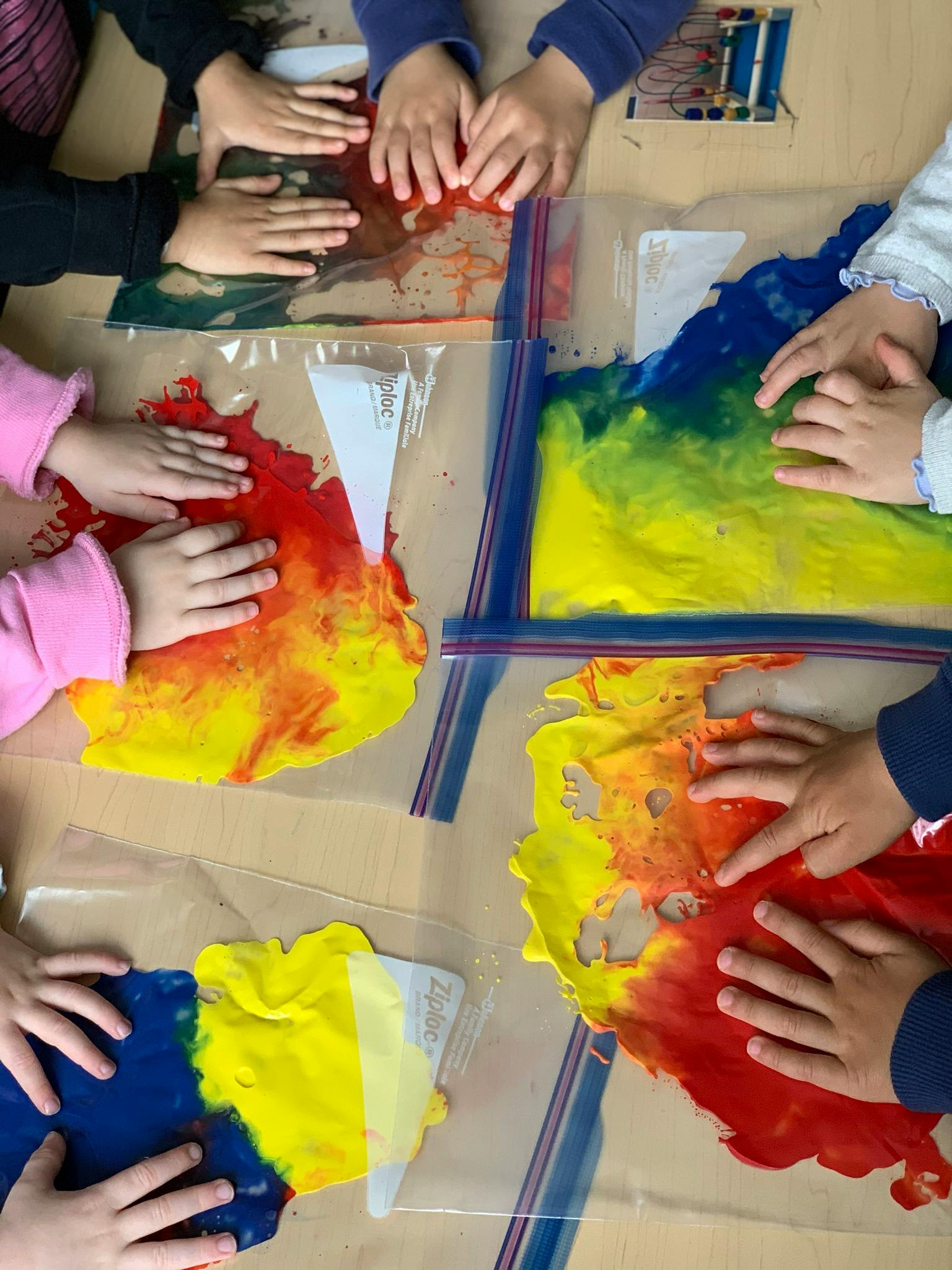 Multiple children's hands pressing on paint in plastic bags