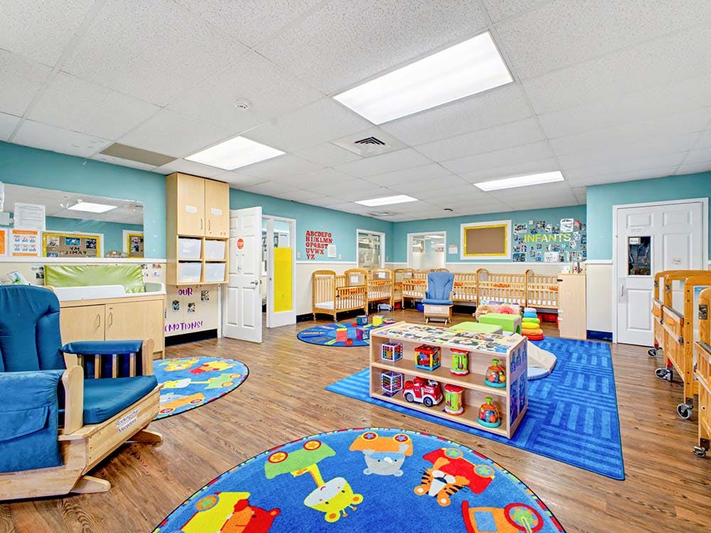 An infant room with multiple cribs, a changing table, and play mats on the floor