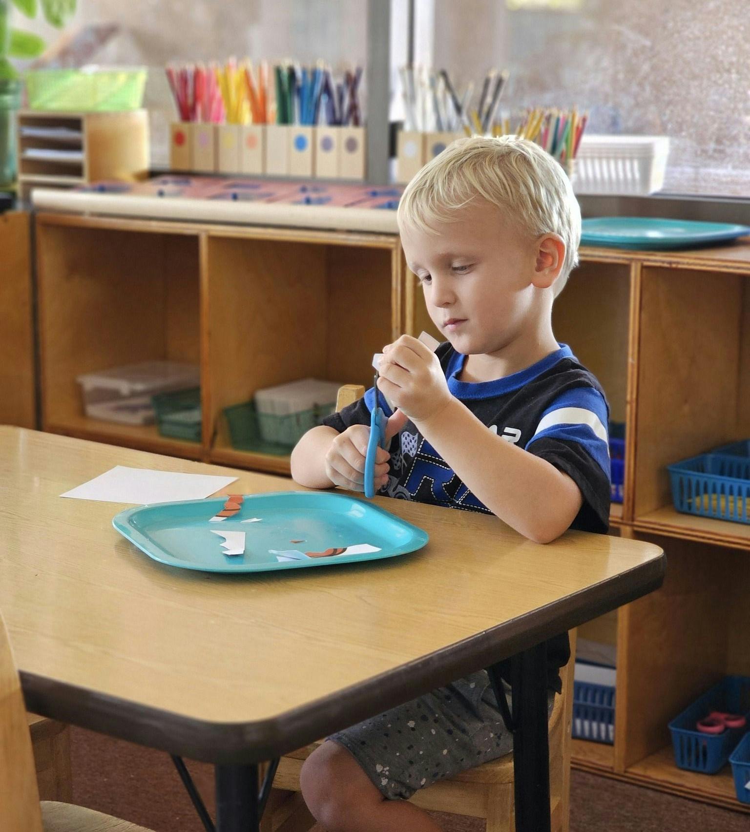 Child at a table cutting paper with scissors