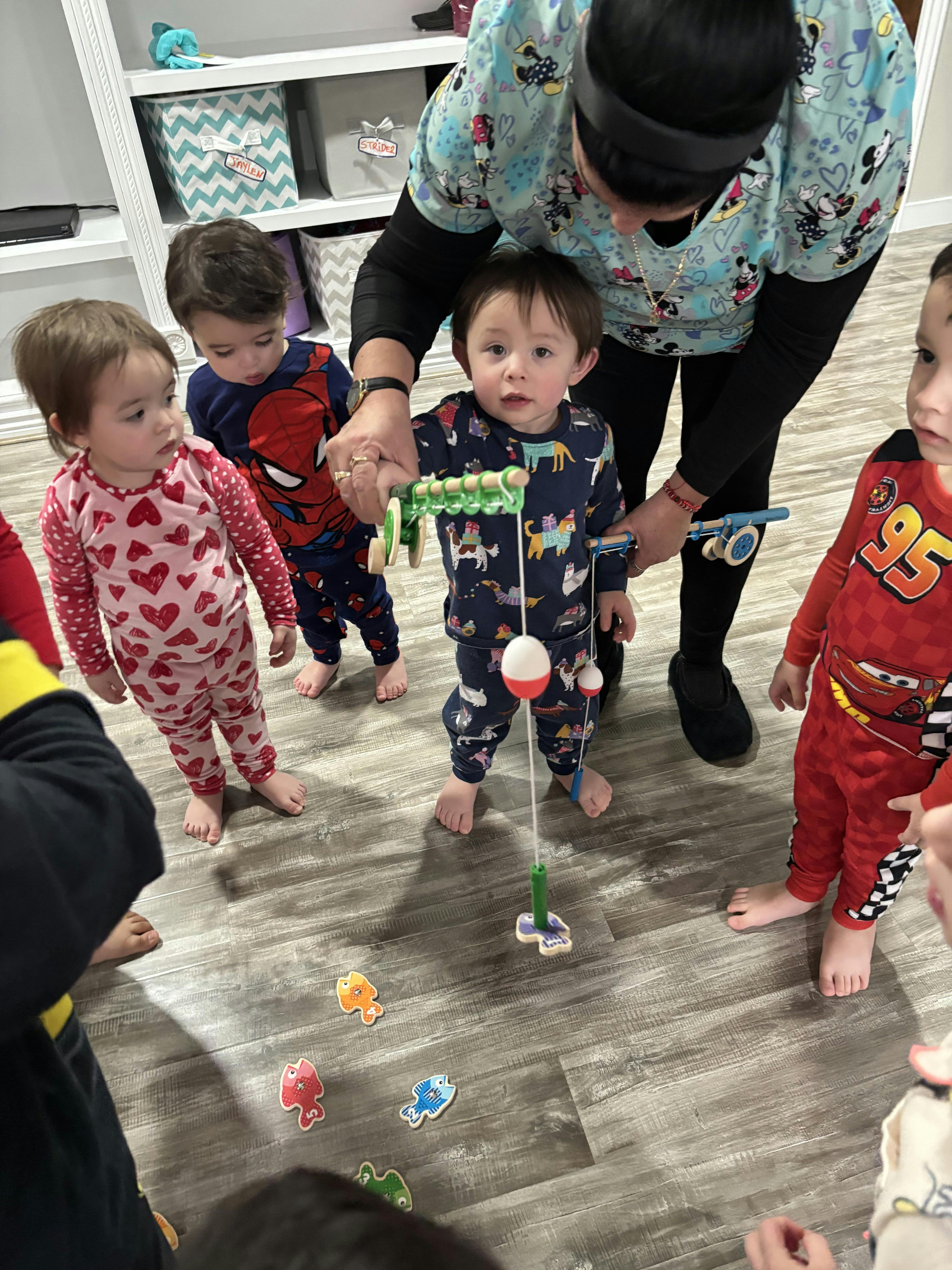 Adult helping a child use a toy fishing rod with other children watching
