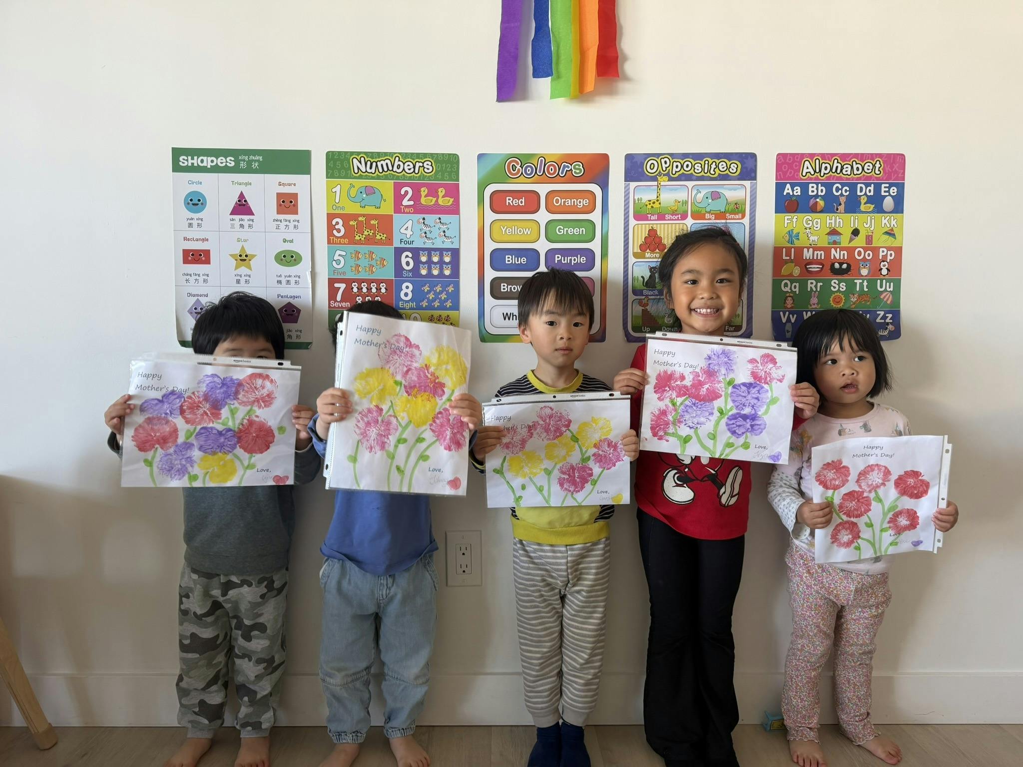Five children holding handmade flower cards in a classroom