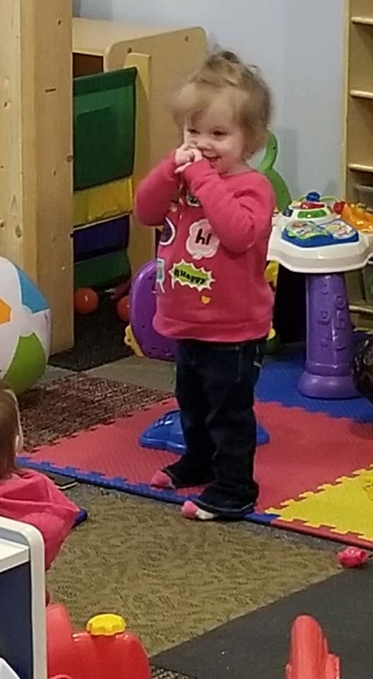 Child standing in a playroom with hands near face