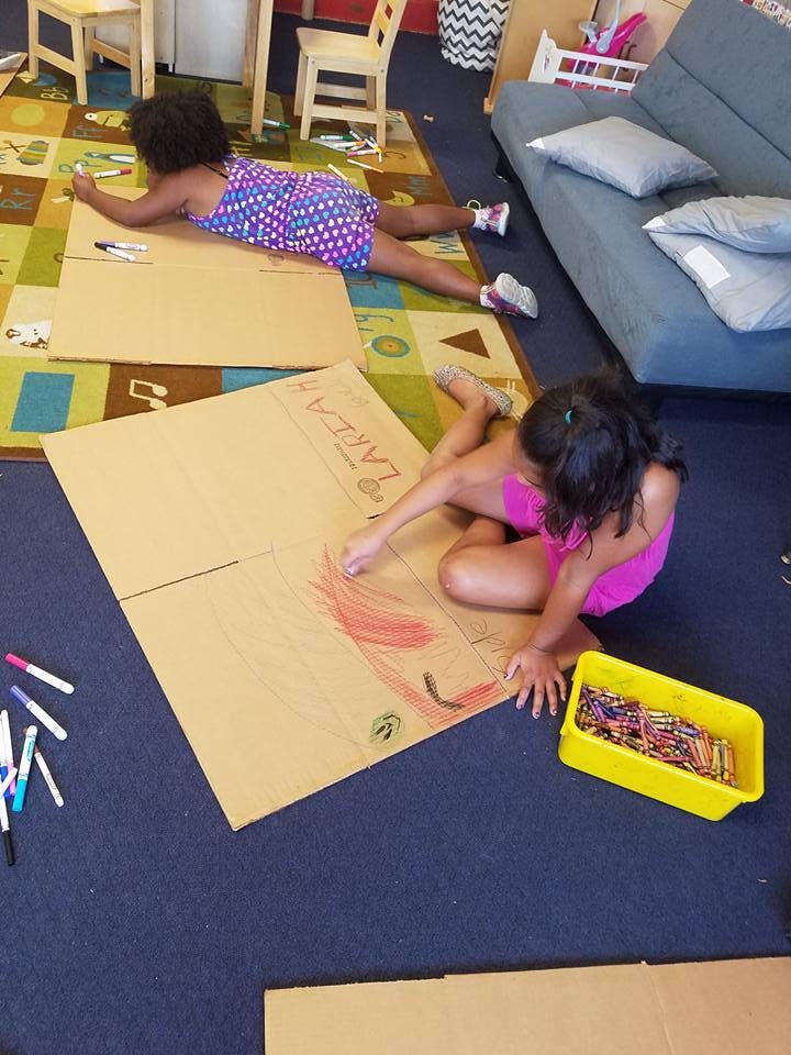 Two children drawing on cardboard boxes on the floor