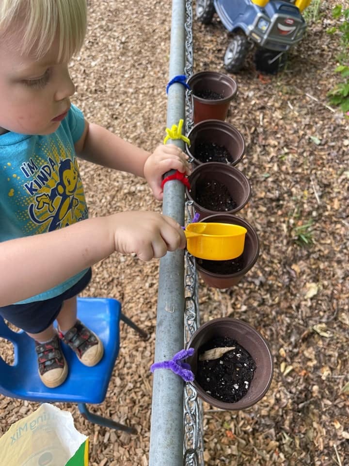 Child on a blue chair playing with a yellow cup and small plant pots