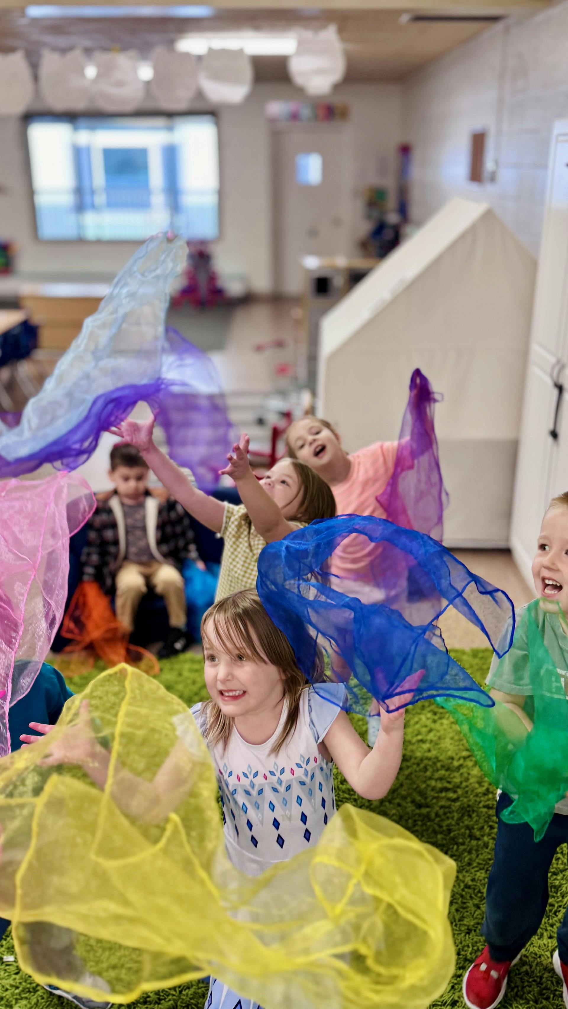 Children playing with colorful sheer fabrics in a classroom