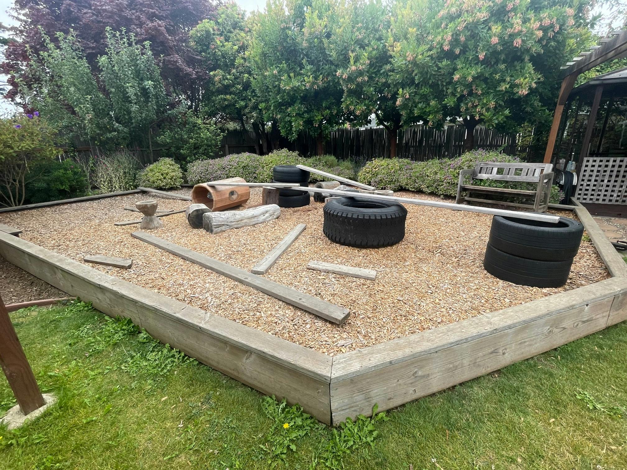 Outdoor play area with tires, wood planks, and gravel