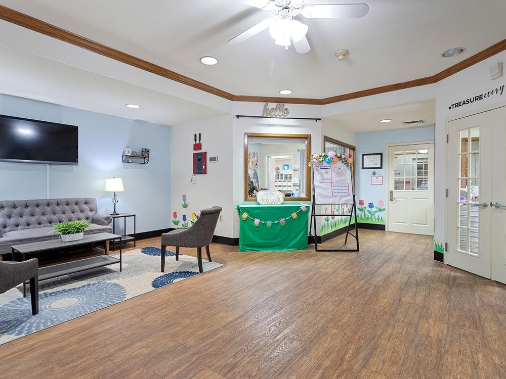 Lobby area with sofa, chairs, TV, and a white board with decorative flowers