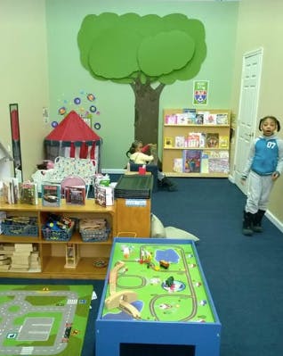 Child standing in a playroom with a large tree mural and toys