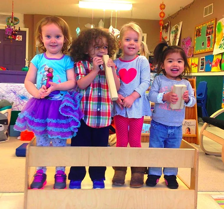 Four children standing behind a wooden barrier, holding objects