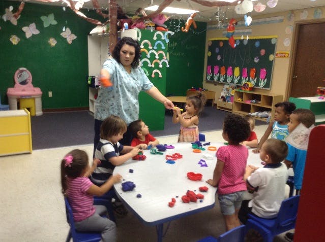 Adult and children gathered around a table with playdough in a classroom