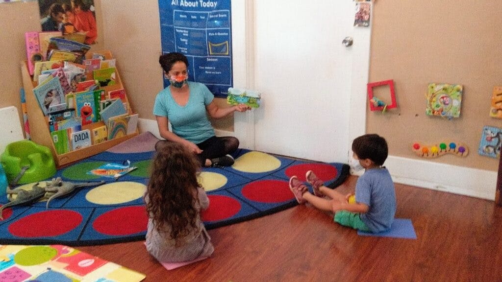 Person sitting on floor with two children in a classroom