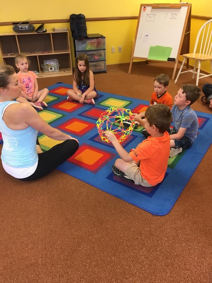 Adult and children sitting on a colorful rug playing with a toy