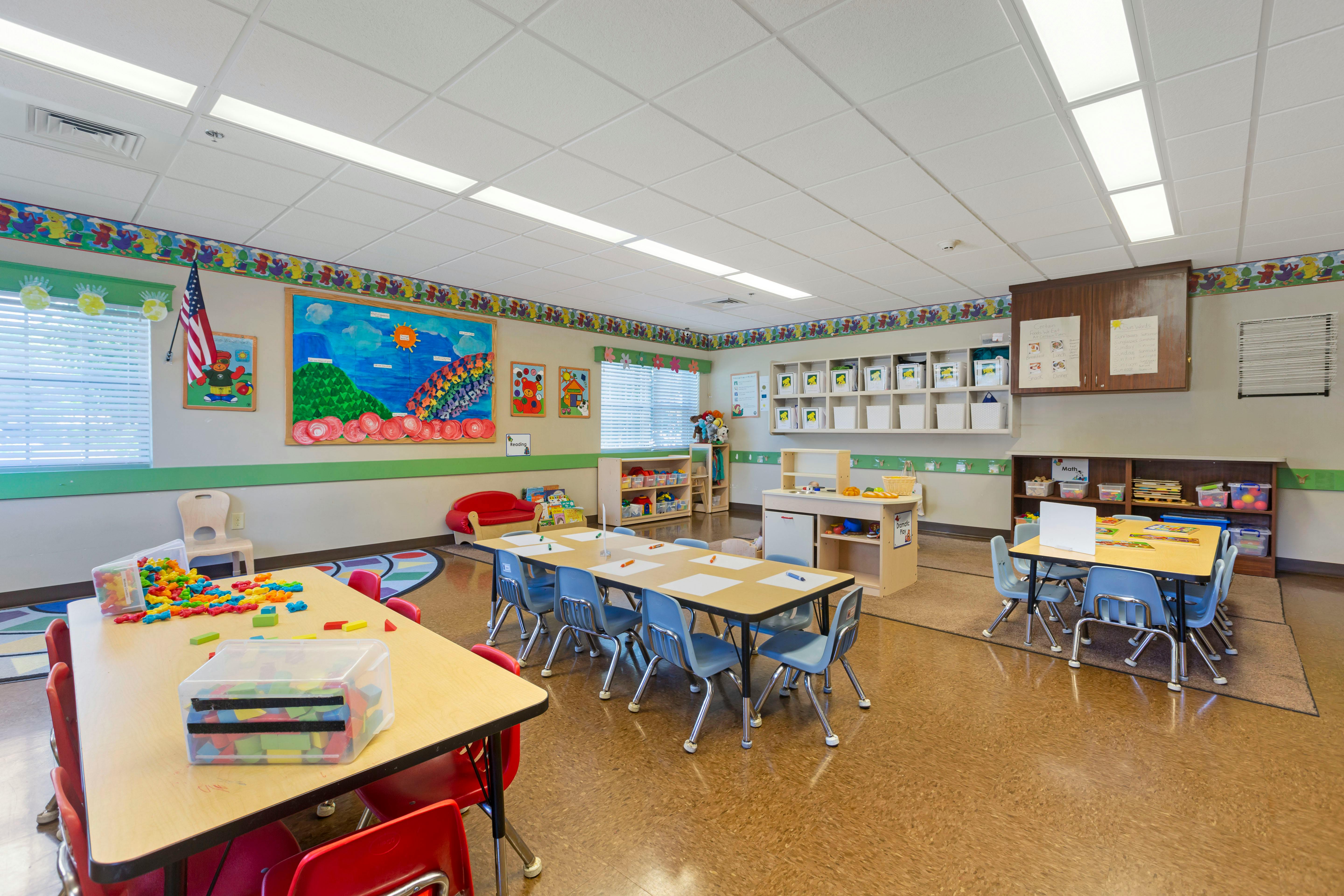 An empty early childhood classroom with multiple tables and chairs
