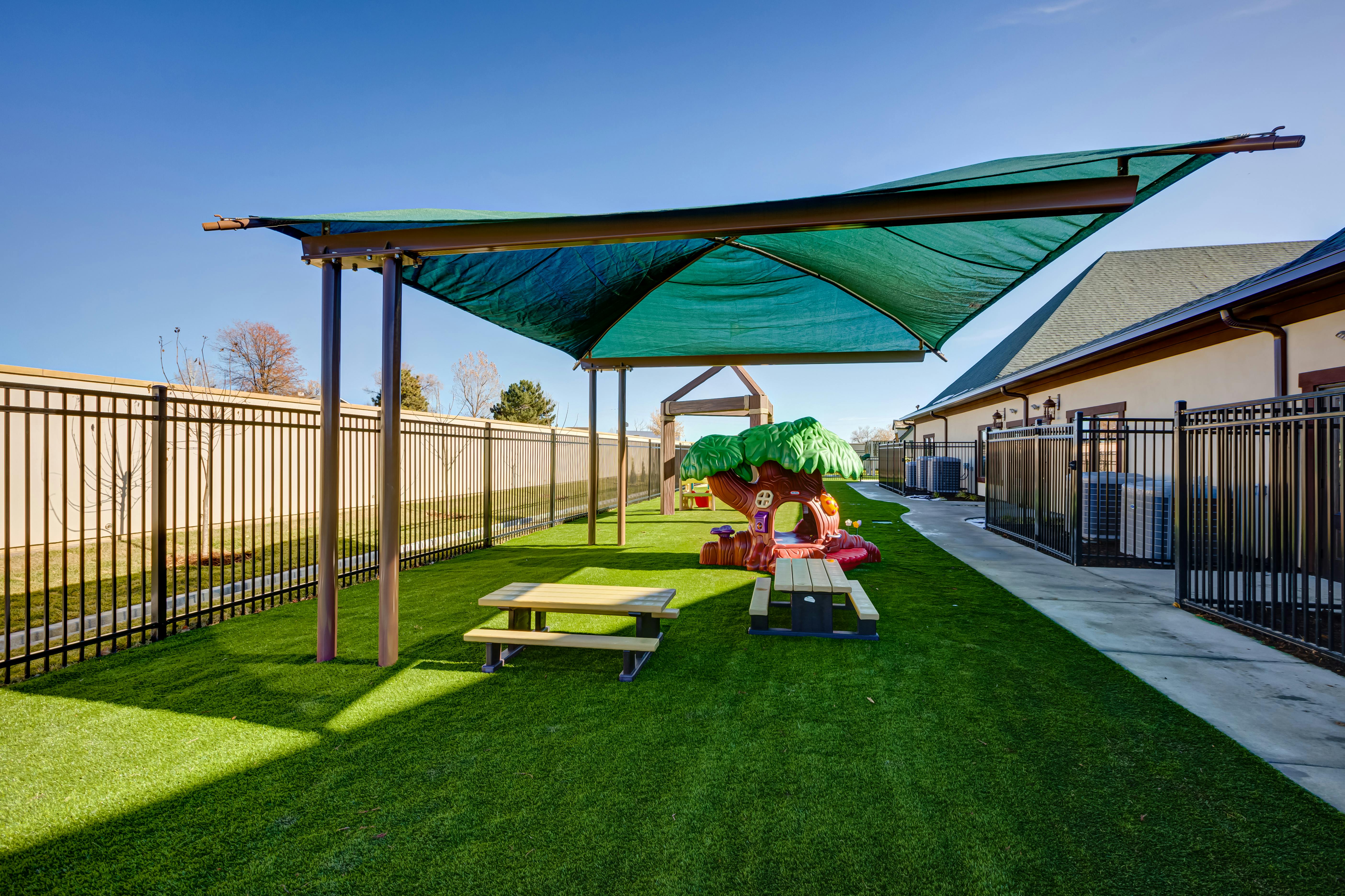 Outdoor playground with artificial turf, shade structure, and play equipment