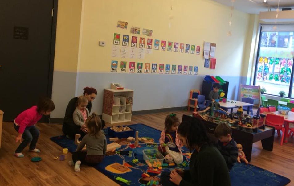 Adults and children playing with toys on a blue rug in a classroom
