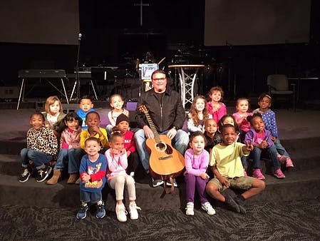 Person with a guitar sitting with a group of children