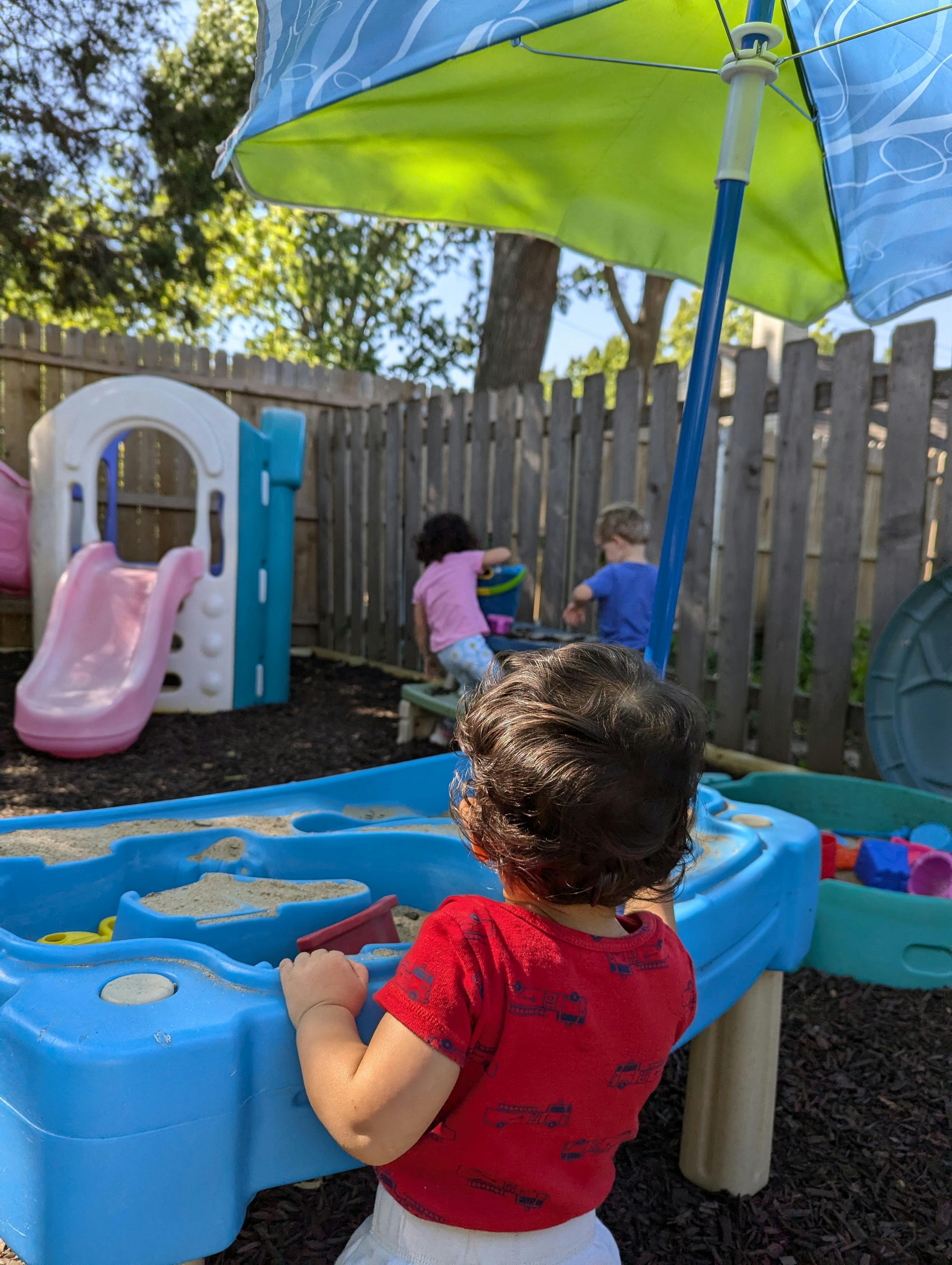 Child playing at a sand and water table with other children in background