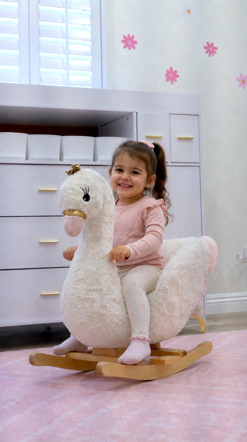 Child sitting on a swan-shaped rocking chair in a room