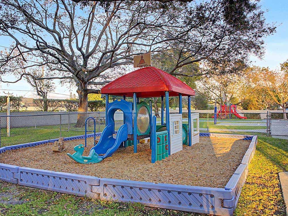 A playground with a red-roofed structure, blue slide, and rocking toys on wood chips