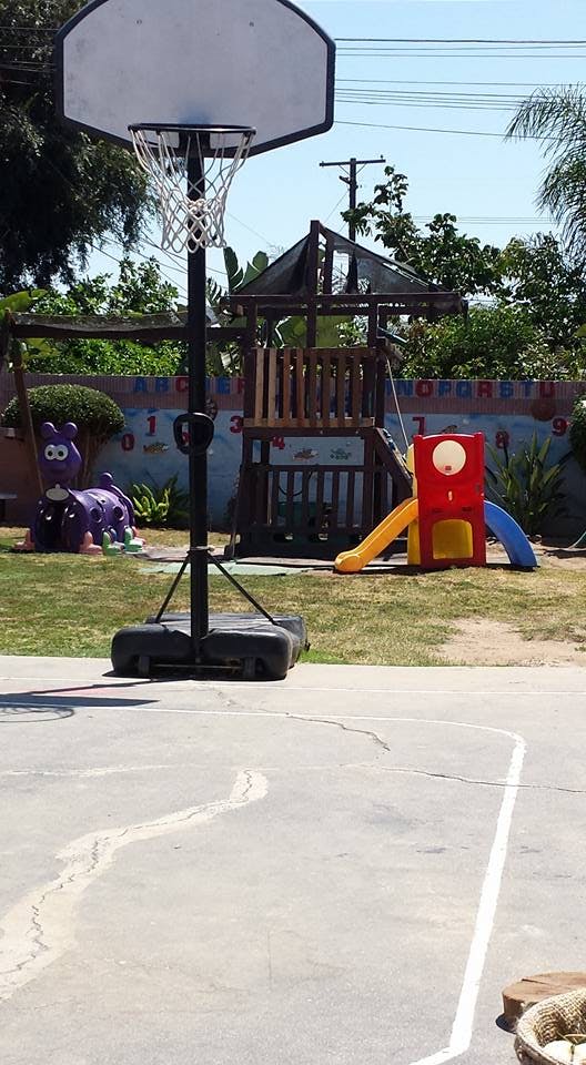 Basketball hoop on a court with a playground in the background