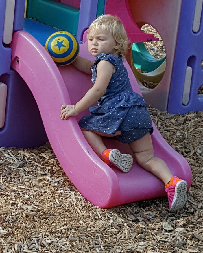 Child climbing up a pink slide on a playground