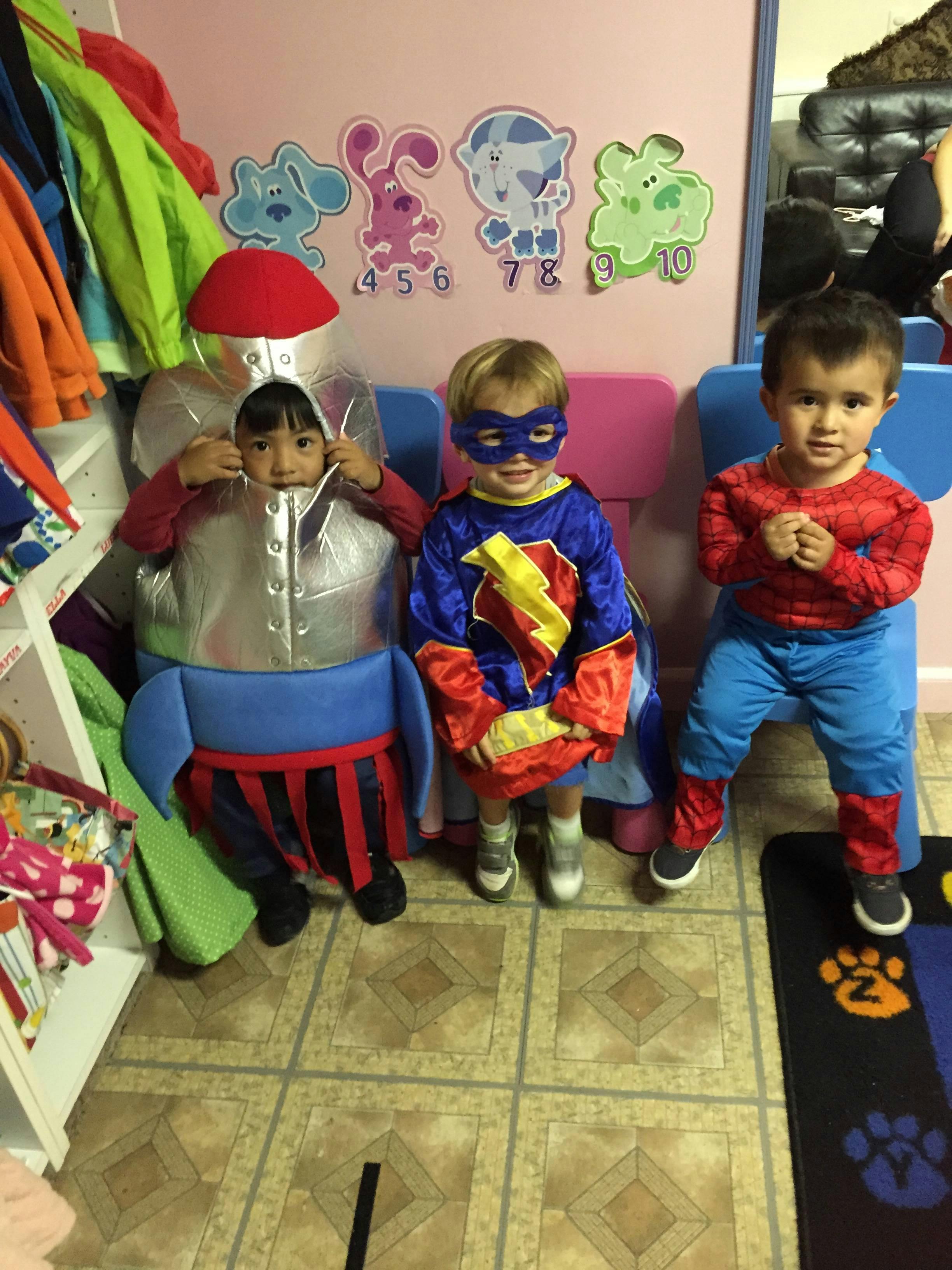 Three children in costumes, one dressed as a robot, one as a superhero, one as Spider-Man
