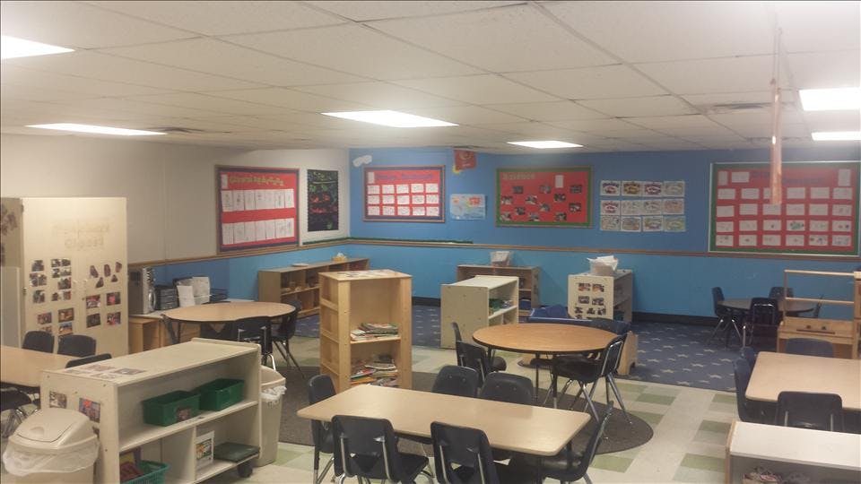An empty classroom with small tables and chairs, shelves, and bulletin boards
