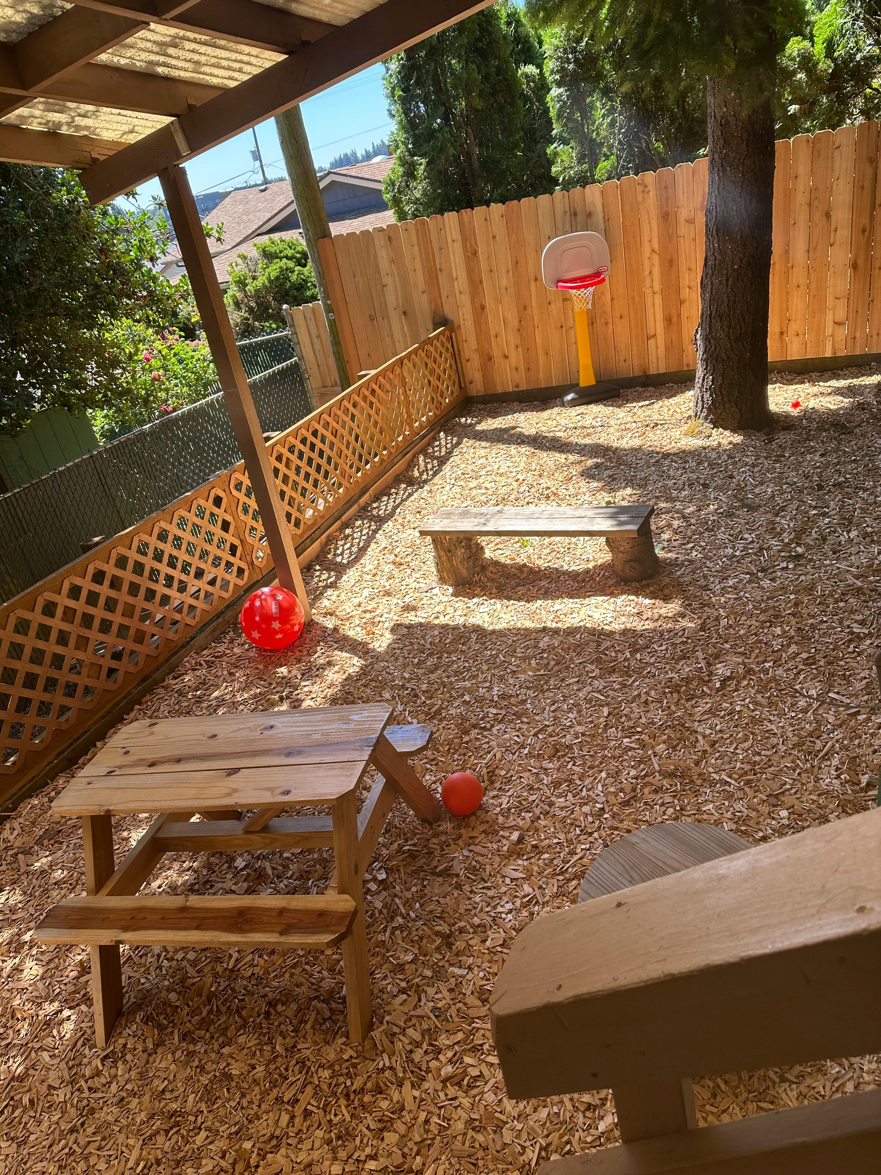 Outdoor play area with wood chips, picnic table, bench, and basketball hoop