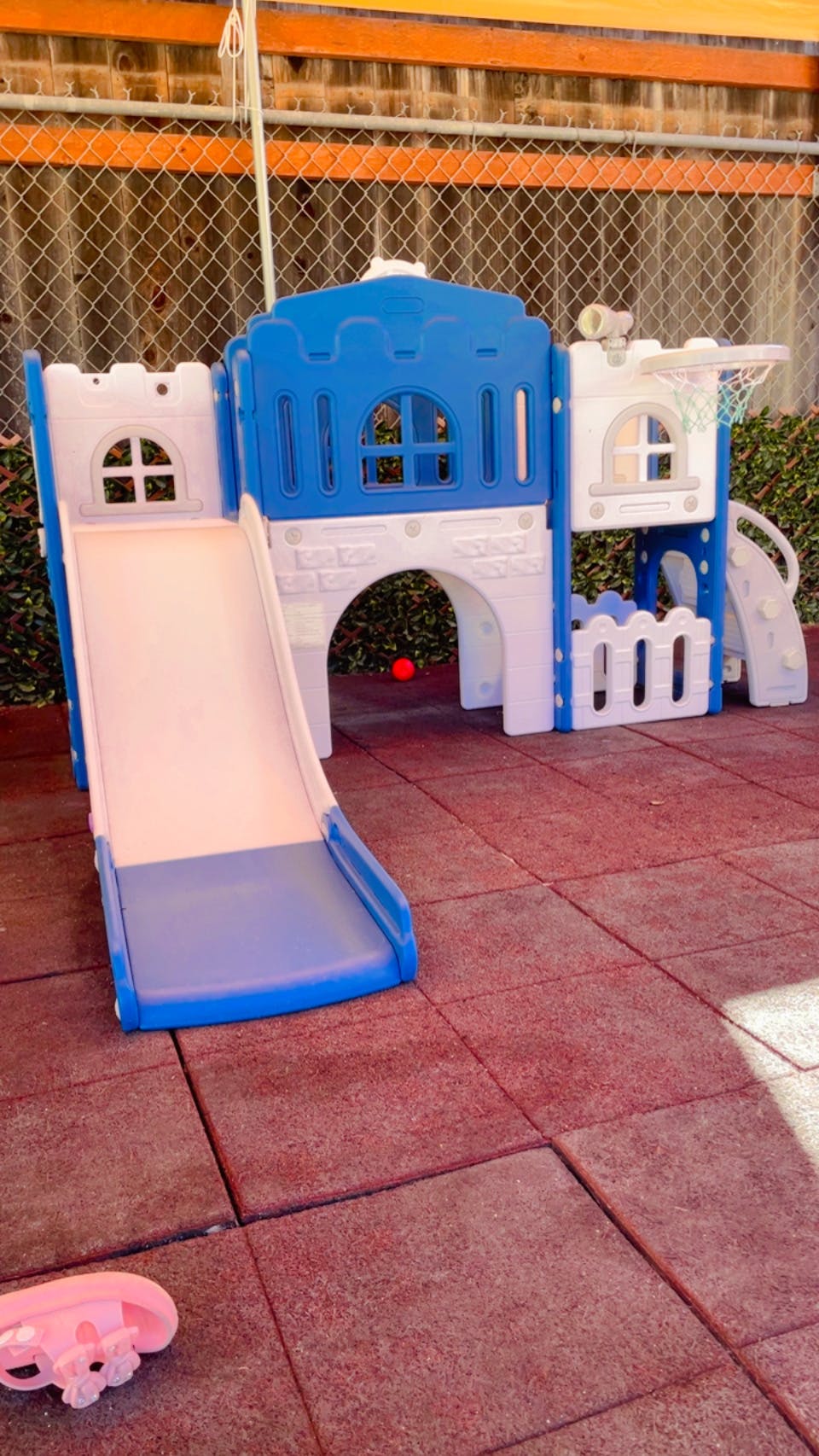 Blue and white plastic play structure with a slide on red playground tiles