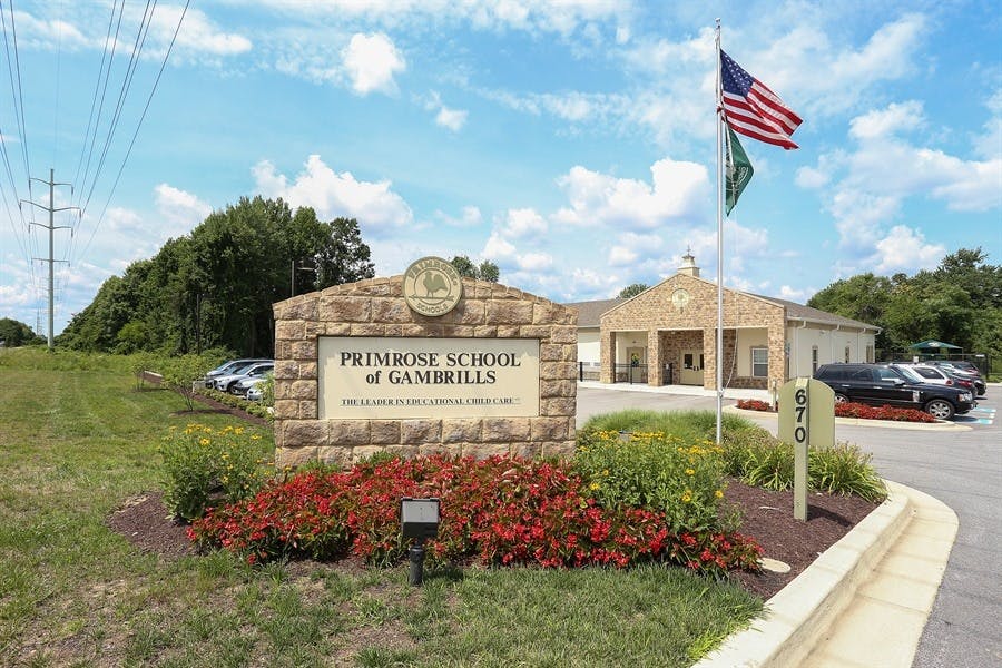 Stone sign for Primrose School of Gaithersburg with building and flags in background