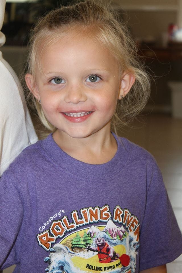 Child smiling and wearing a purple t-shirt with "Rolling River" text