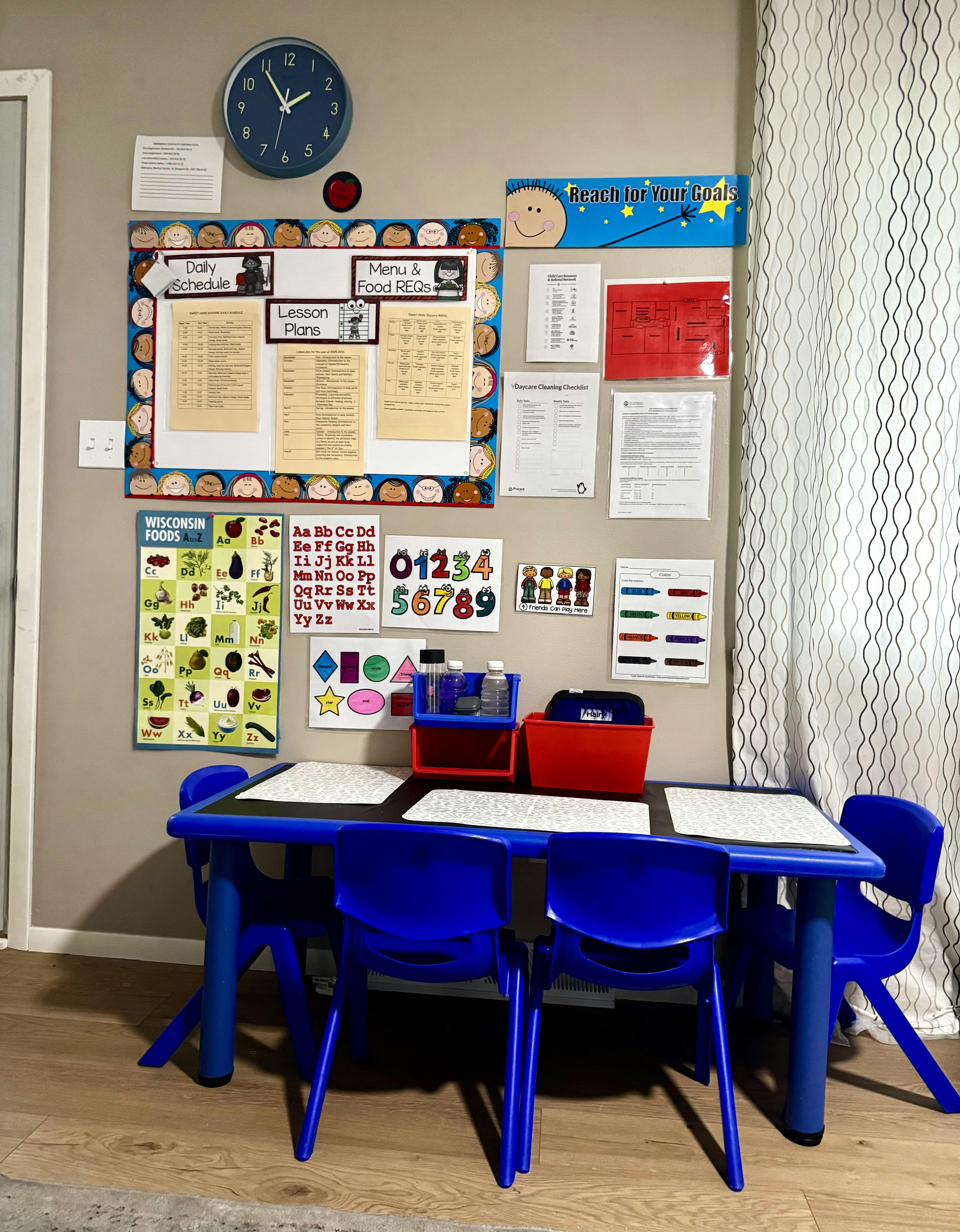 Classroom wall with schedules and educational posters above a table with four blue chairs