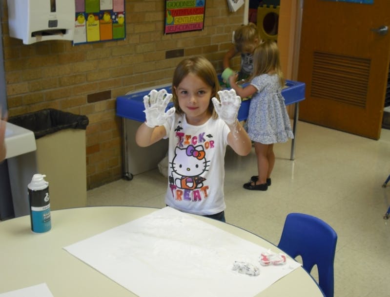Child with white paint on hands in a classroom