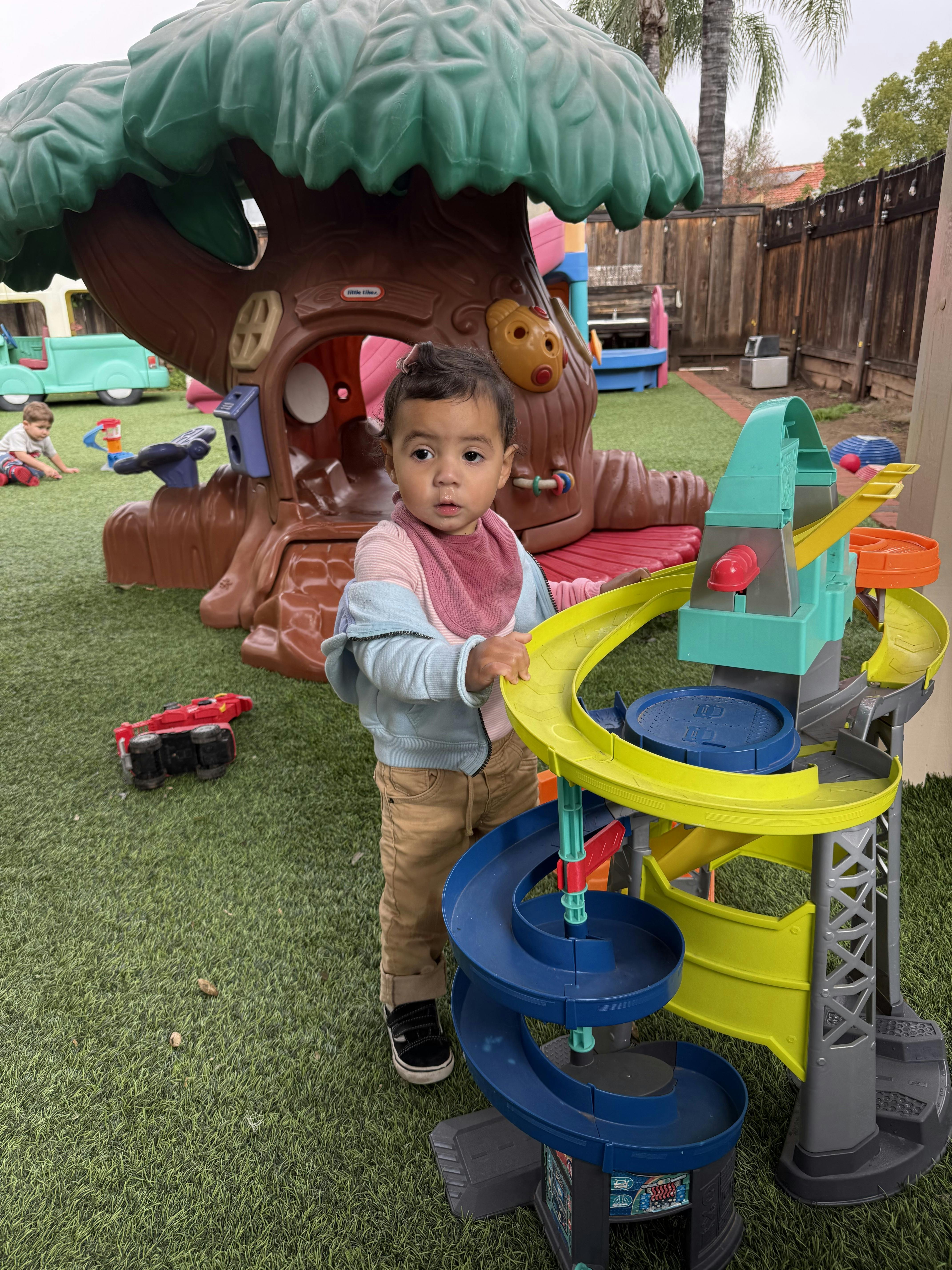 Child standing on artificial grass next to a colorful toy car ramp