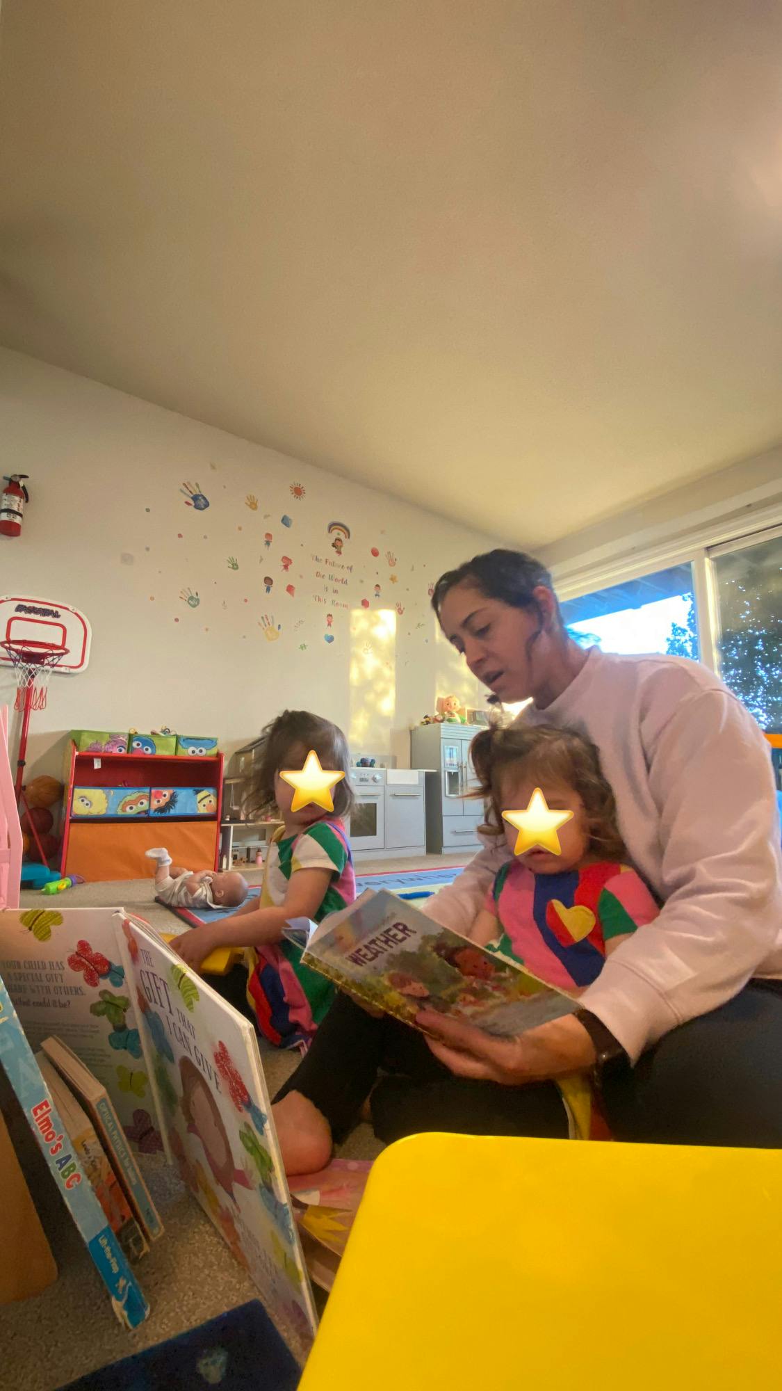 Person reading to two children in a playroom with books around them