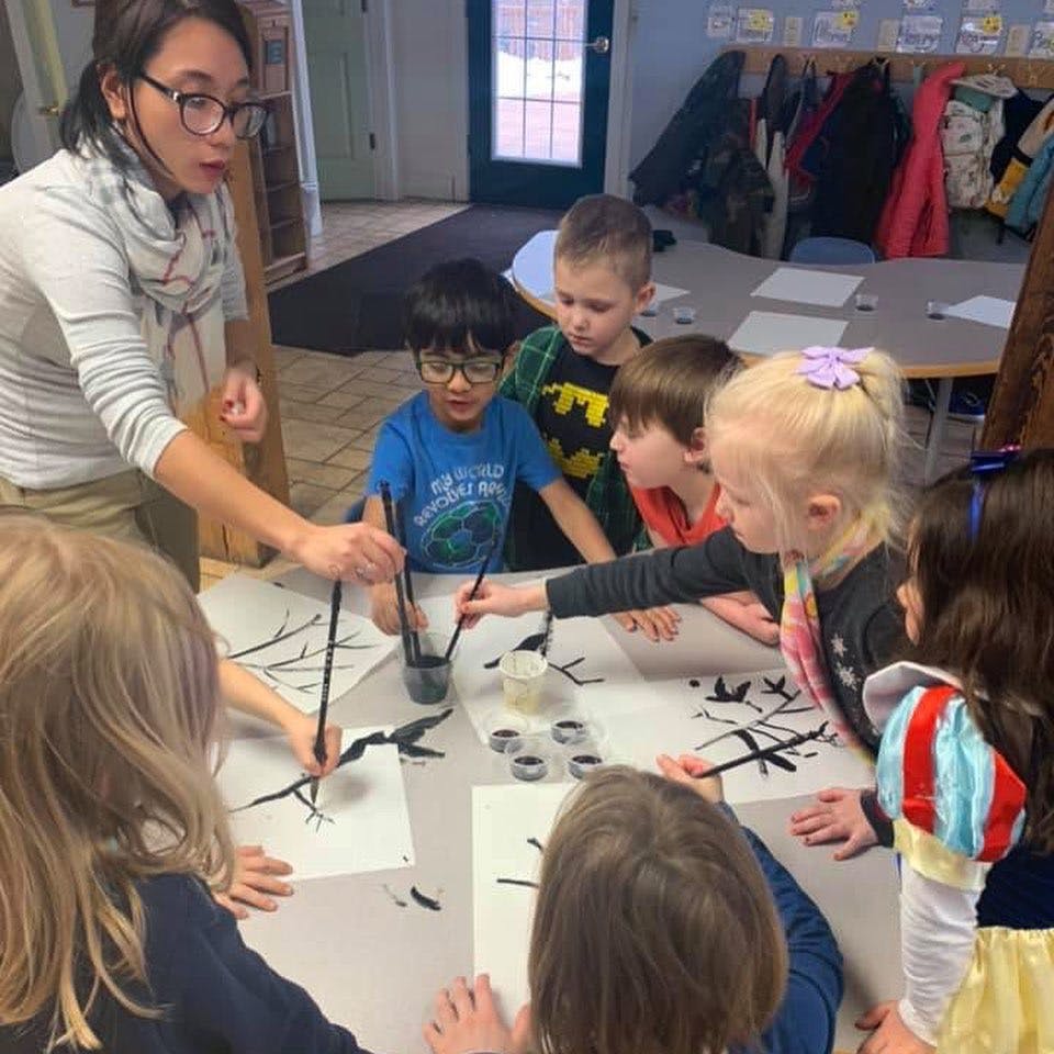 Adult person and children painting with brushes at a table