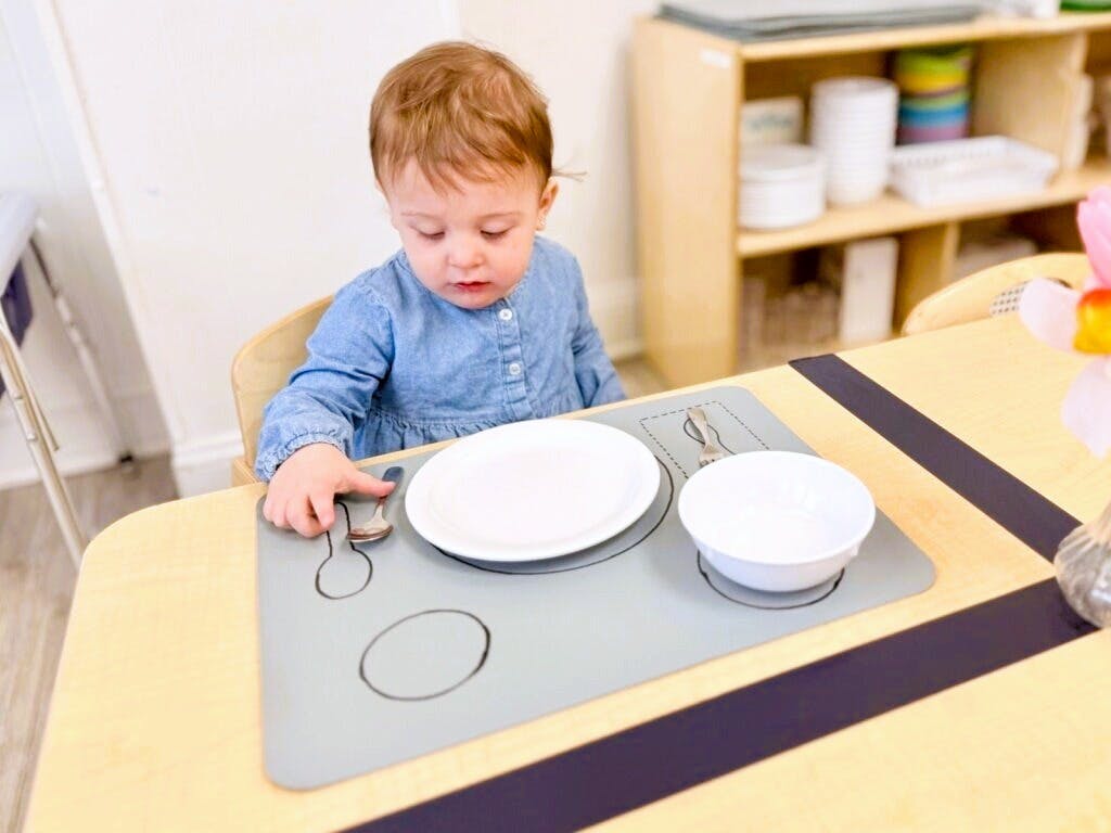 Child setting a spoon on a placemat with drawn utensil outlines