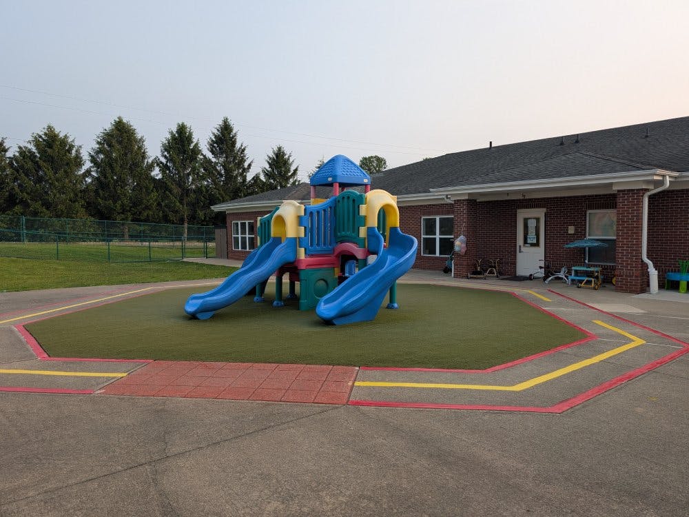 Colorful playground structure on artificial turf with a brick building in background
